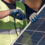 Worker in a safety vest and gloves securing a solar panel with a screwdriver