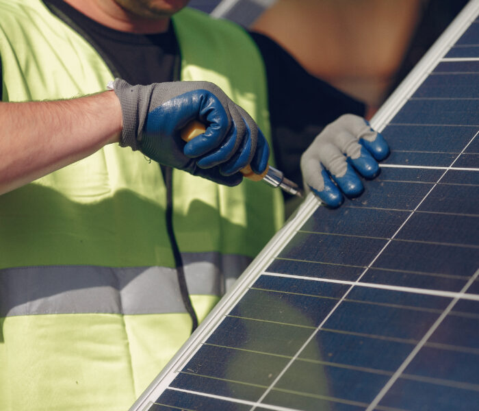 Worker in a safety vest and gloves securing a solar panel with a screwdriver