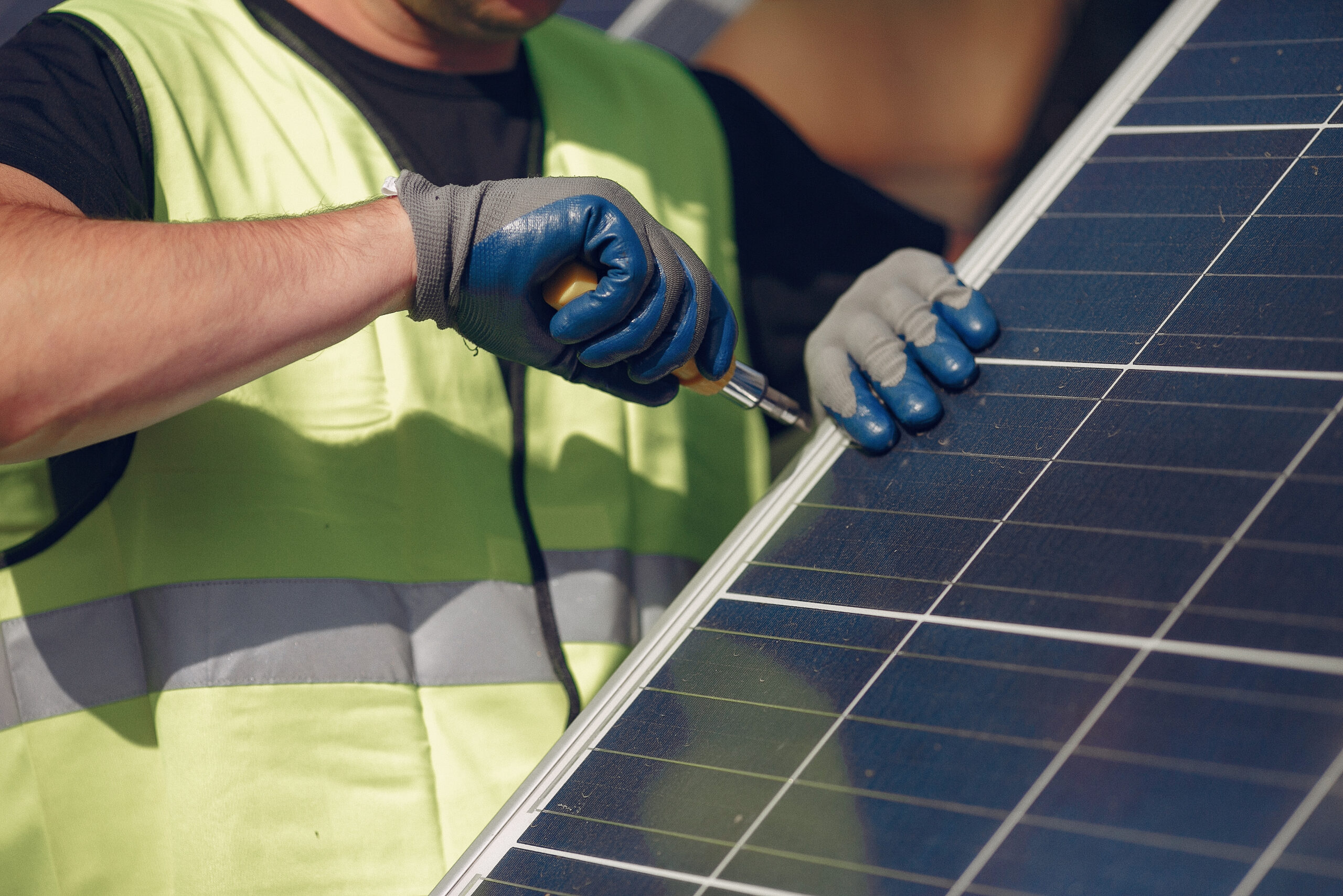 Worker in a safety vest and gloves securing a solar panel with a screwdriver